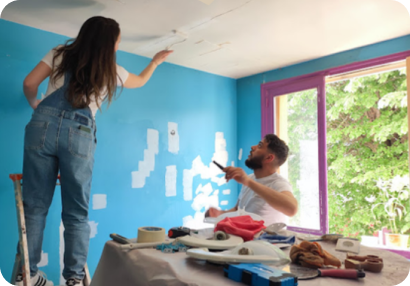 Deux bénévoles rebouchent et préparent les murs bleus d’une pièce avant de la repeindre