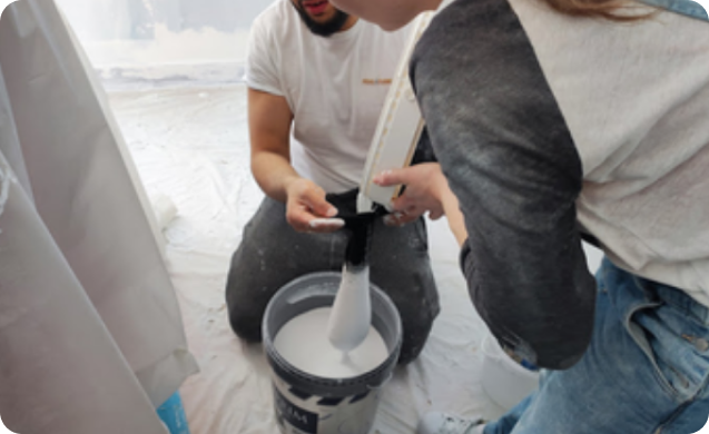 Deux bénévoles préparent la peinture blanche en trempant un rouleau dans le seau