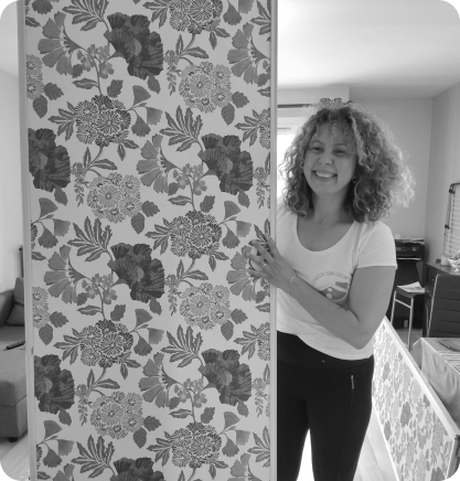 Une bénévole souriante tient un panneau de papier peint à motifs floraux dans un logement